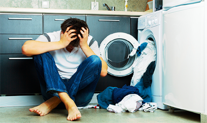 Nešťastný muž sedí pri otvorenej práčke s vysypaným prádlom.